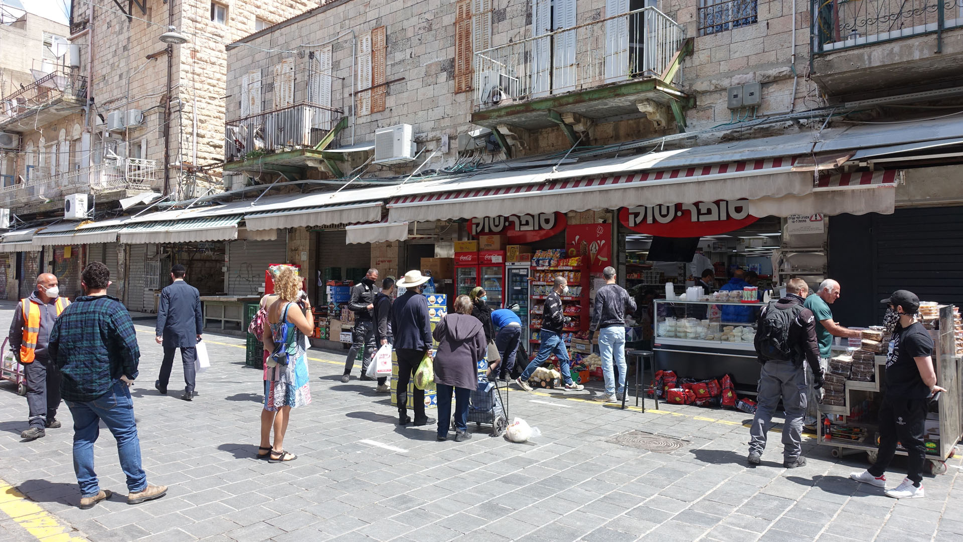 Auf dem Schuk Mahane Jehuda drängen sich in normalen Zeiten viele Besucher. Hier halten Kunden vor einem Minimarkt auf dem Schuk den Mindestabstand ein.