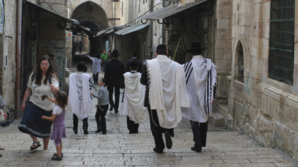 Woher kommt das Wort Jude? Bild: Jüdische Männer mit Gebetsschal (Tallit) in der Jerusalemer Altstadt Die hebräische Bezeichnung für einen Juden lautet „jehudi“. Dieses Wort leitet sich vom Namen des vierten Sohnes vom Stammvater Jakob ab – Jehuda. Die Bezeichnung „jehudi“ bezog sich zunächst nur auf dessen Nachkommen, also Mitglieder des Stammes Juda. Nach der Teilung des zuvor von König Salomo regierten Staatsgebietes hieß das Nordreich Israel – ein Beiname Jakobs – und das Südreich Juda. Später wurde das Gebiet südlich von Jerusalem als „Jehuda“ bekannt, die deutsche Übersetzung ist „Judäa“. Die Bezeichnung „Palästina“ führte der römische Kaiser Hadrian im Jahr 135 ein. Der Begriff „Jude“ bezeichnet einerseits eine ethnische Abstammung, die seit der römischen Zeit über die Mutter bestimmt wird. Andererseits bezieht er sich auf eine Glaubensrichtung. Ein Übertritt zum Judentum geschieht bei Männern durch Beschneidung, das Untertauchen im rituellen Tauchbad und ein Glaubensbekenntnis. Frauen reinigen sich nur im Tauchbad und bekennen ihren neuen Glauben. Ihre Kinder sind ebenfalls Juden.