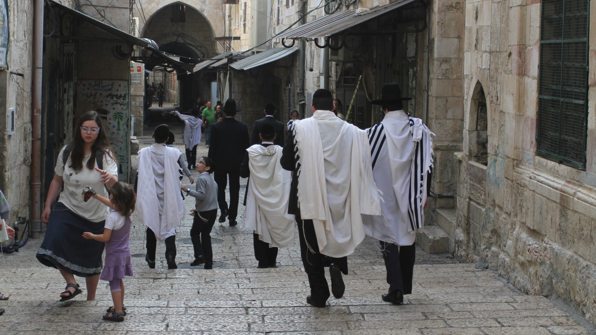 Woher kommt das Wort Jude? Bild: Jüdische Männer mit Gebetsschal (Tallit) in der Jerusalemer Altstadt Die hebräische Bezeichnung für einen Juden lautet „jehudi“. Dieses Wort leitet sich vom Namen des vierten Sohnes vom Stammvater Jakob ab – Jehuda. Die Bezeichnung „jehudi“ bezog sich zunächst nur auf dessen Nachkommen, also Mitglieder des Stammes Juda. Nach der Teilung des zuvor von König Salomo regierten Staatsgebietes hieß das Nordreich Israel – ein Beiname Jakobs – und das Südreich Juda. Später wurde das Gebiet südlich von Jerusalem als „Jehuda“ bekannt, die deutsche Übersetzung ist „Judäa“. Die Bezeichnung „Palästina“ führte der römische Kaiser Hadrian im Jahr 135 ein. Der Begriff „Jude“ bezeichnet einerseits eine ethnische Abstammung, die seit der römischen Zeit über die Mutter bestimmt wird. Andererseits bezieht er sich auf eine Glaubensrichtung. Ein Übertritt zum Judentum geschieht bei Männern durch Beschneidung, das Untertauchen im rituellen Tauchbad und ein Glaubensbekenntnis. Frauen reinigen sich nur im Tauchbad und bekennen ihren neuen Glauben. Ihre Kinder sind ebenfalls Juden.